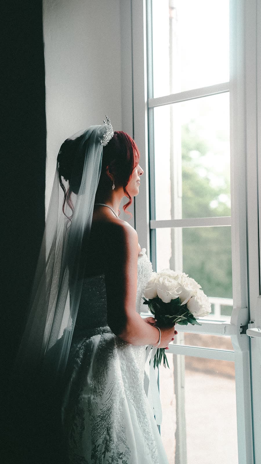 La mariée devant la fenêtre, voile et bouquet