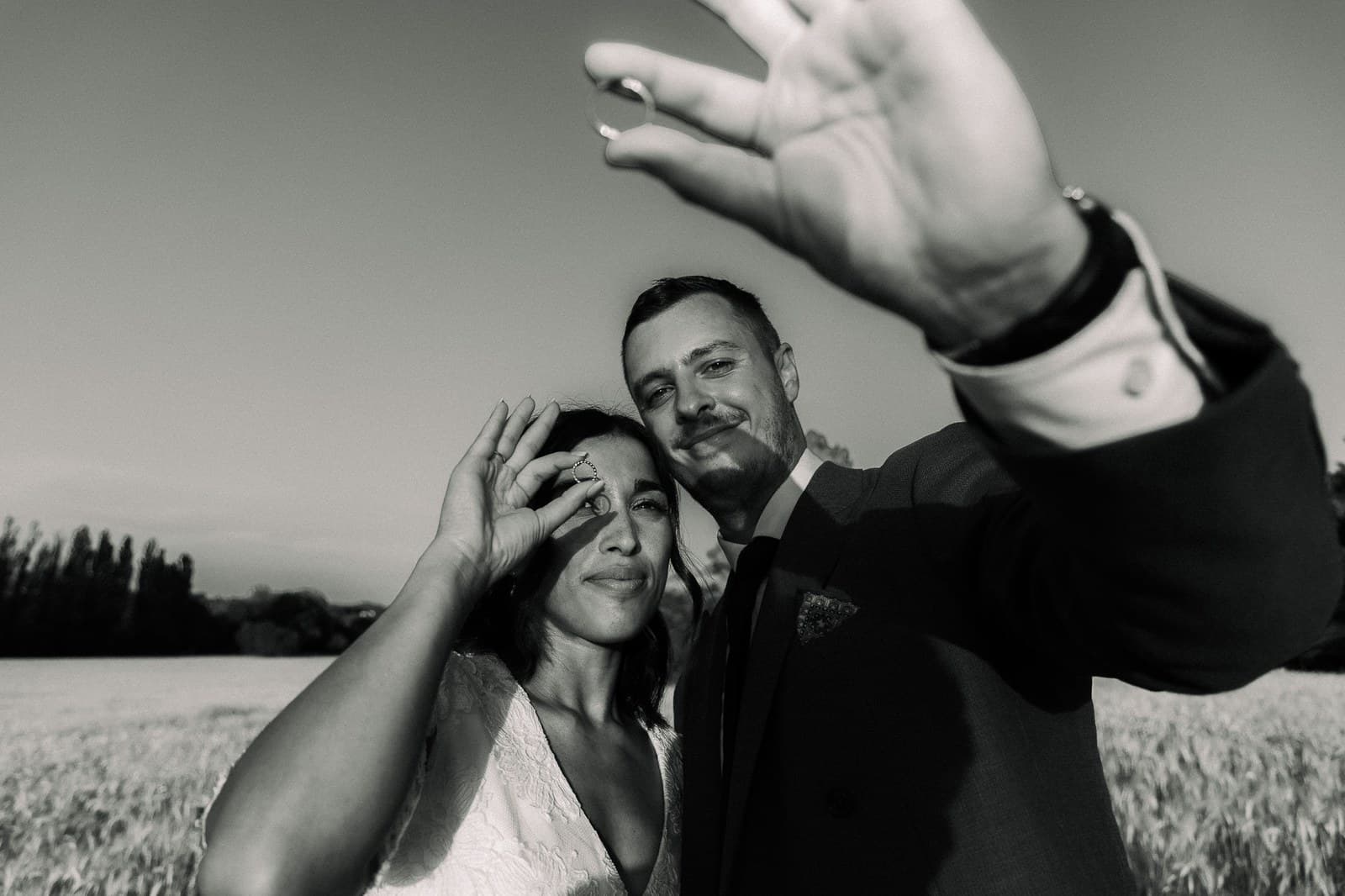 Le marié écarte la main devant l’objectif, la mariée rit contre lui